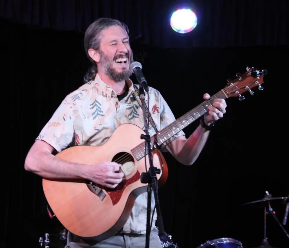 Fish on stage with an acoustic guitar, mid-shout